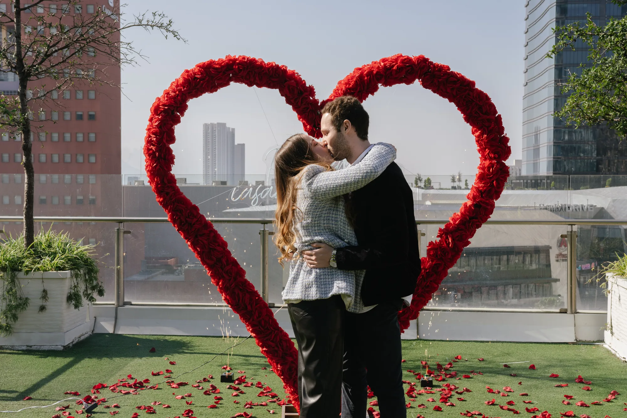 Pareja besándose dentro de un arco de rosas rojas con la ciudad de Monterrey al fondo